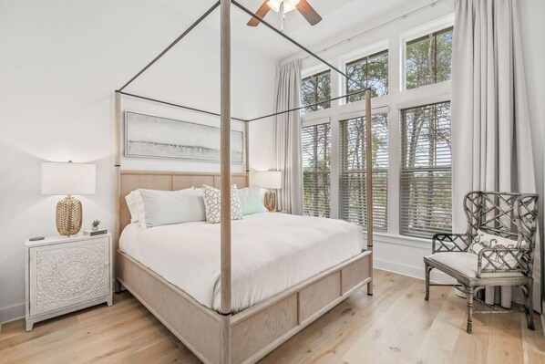 A four-poster bed with a wooden frame, a nightstand with a woven lamp, and a chair with a woven backrest.