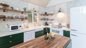Una cocina con encimeras de madera, armarios verdes, microondas, estufa y repisas con utensilios de cocina.