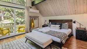 Un dormitorio con un ventanal grande, una cama con ropa de cama estampada, un banco y una maleta.
