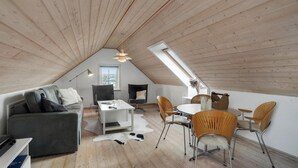 A spacious loft with a sloped ceiling, a dining area with a round table and chairs, a gray sofa, and a large window providing natural light. - 3 bedroom gorgeous home in Vestervig (Vestervig)