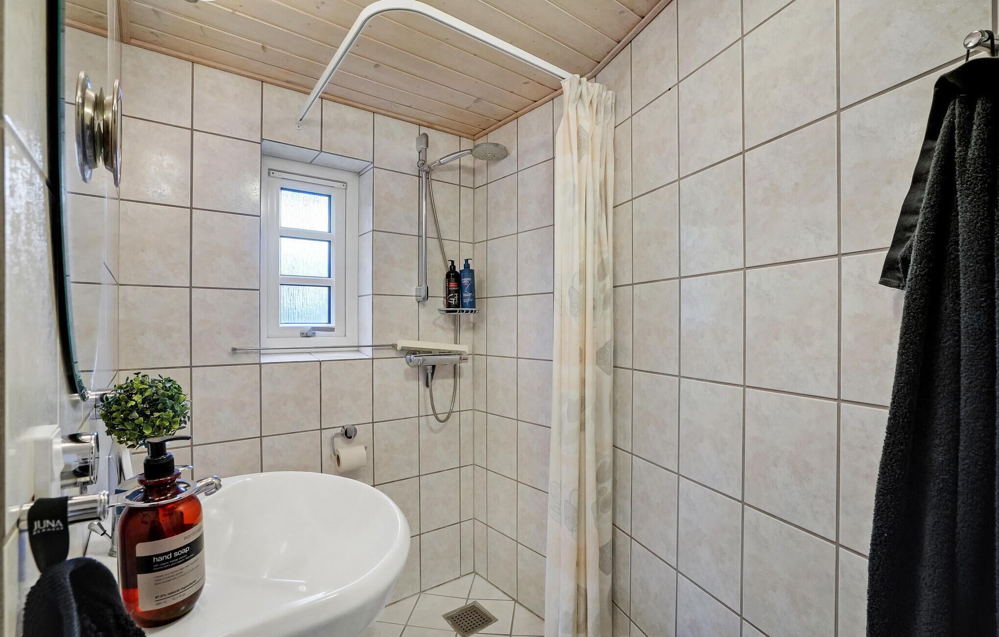 Un baño con lavamanos blanco, ducha y ventana.