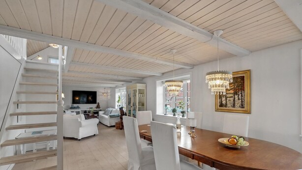 A spacious living area with a wooden staircase, a dining table with chairs, a chandelier, and a television. - 3 bedroom gorgeous home in Vestervig (Vestervig)
