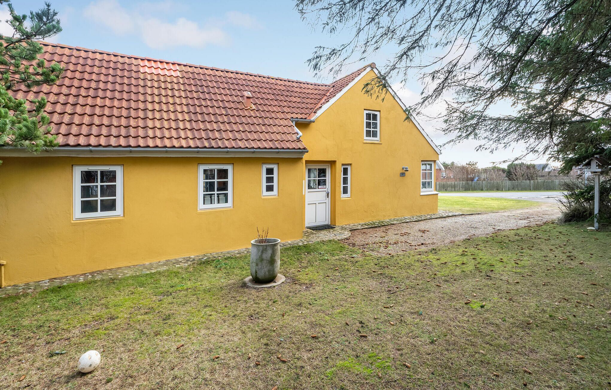 A yellow building with a red-tiled roof, a small front porch, and a grassy yard.
