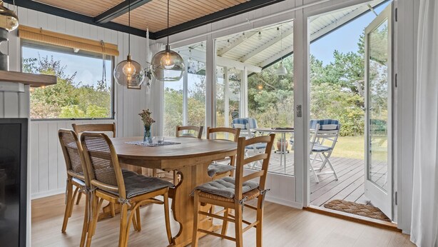 A dining area with a wooden table and chairs, large windows, and hanging pendant lights. - 3 bedroom awesome home in Skjern (Skjern)