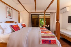 A four-poster bed with a colorful quilt, a wooden headboard, and a view of a tropical garden through an open door. - Magnificent 5 Br Villa with pool: amazing views (Puna'auia)