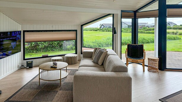 Un salón moderno con un televisor grande, asientos cómodos y vistas a un paisaje verde.