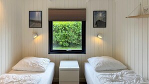 Una habitación con dos camas, una ventana con vistas a zonas verdes y lámparas fijadas a la pared.