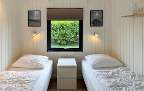 Een kamer met twee bedden, een raam met uitzicht op groen en wandlampen.