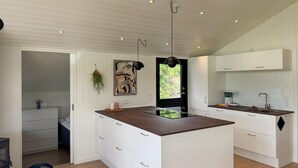 Una cocina moderna con armarios blancos, una isla central con encimera oscura, iluminación colgante y vistas por una ventana.