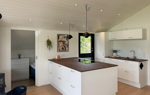 Une cuisine moderne avec des meubles blancs, un îlot central doté d’un plan de travail foncé, des luminaires suspendus et une vue par une fenêtre.