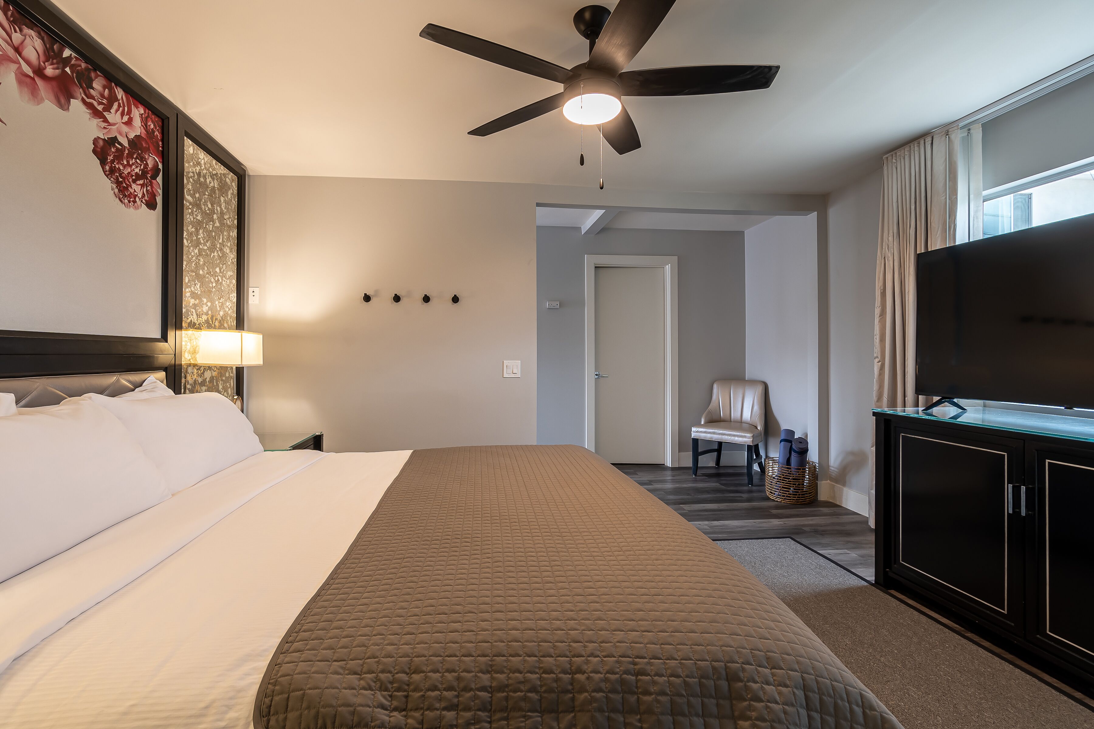 Une chambre d’hôtel avec un grand lit, un ventilateur de plafond, une télévision et une vue sur le couloir.