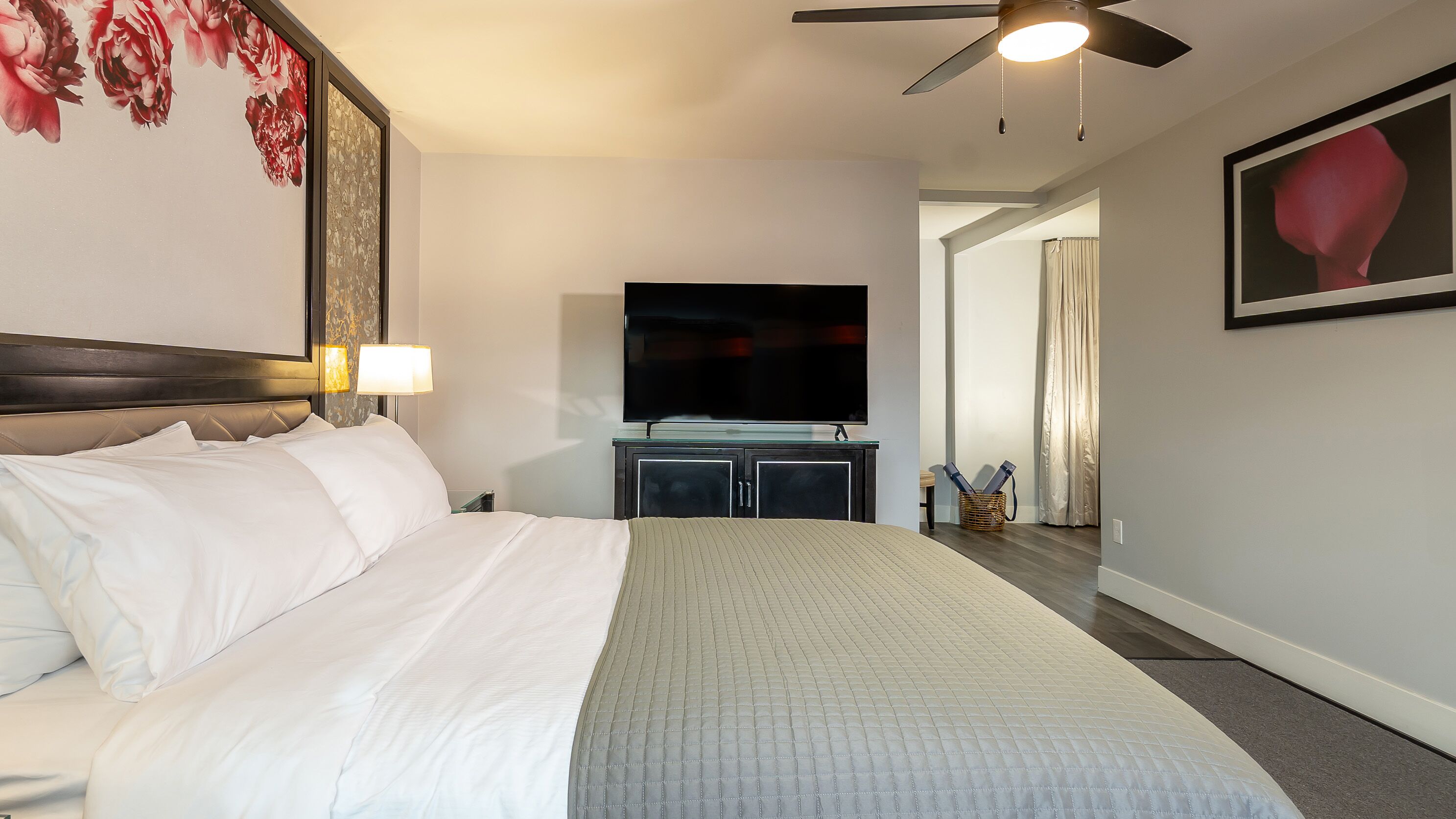 A hotel room with a large bed, a flat-screen TV, a ceiling fan, and a painting on the wall.
