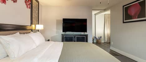 A hotel room with a large bed, a flat-screen TV, a ceiling fan, and a painting on the wall.