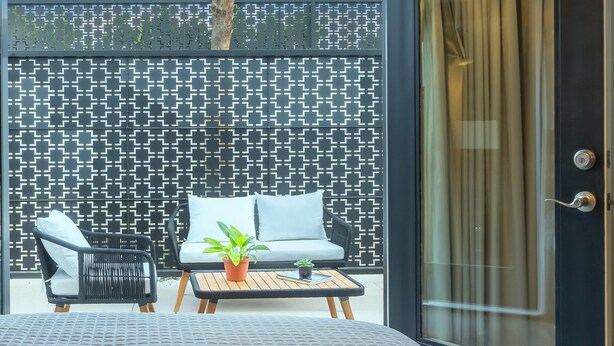 A modern outdoor seating area with two chairs and a small table, a potted plant, and a patterned wall. - Onsen Hotel & Spa (Desert Hot Springs)