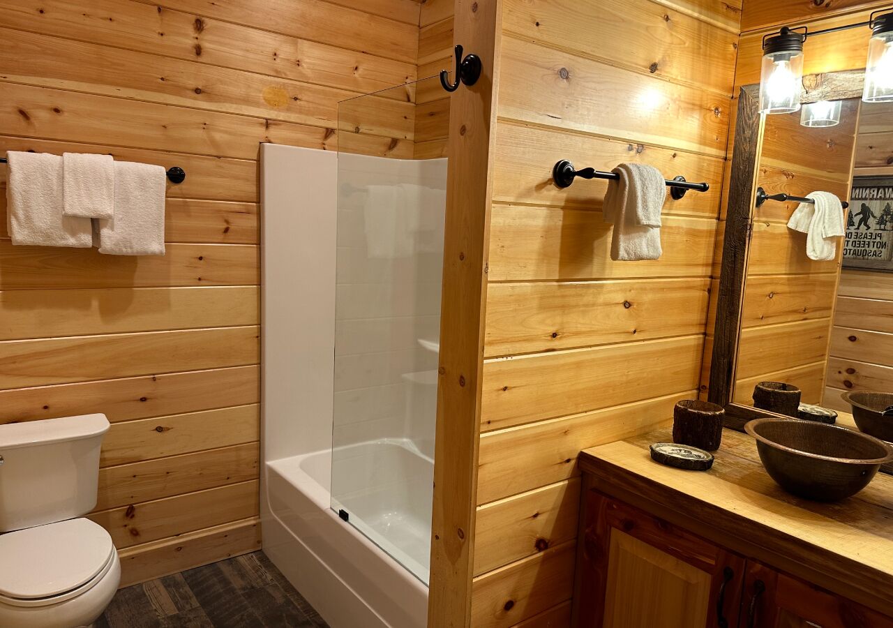 Une salle de bain aux murs lambrissés, équipée d’une baignoire, de toilettes et d’un meuble-lavabo avec un miroir et un porte-serviettes.