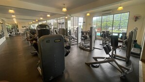 A gym with various exercise machines, large windows, and hanging lights.