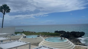 A beachside resort with multiple hot tubs and lounge chairs, overlooking the ocean.