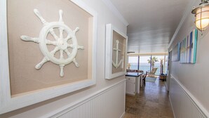 Un couloir décoré sur le thème de la marine, avec notamment des roues de navire accrochées aux murs, une vue sur l’océan par une grande fenêtre et un coin repas avec des sièges extérieurs.