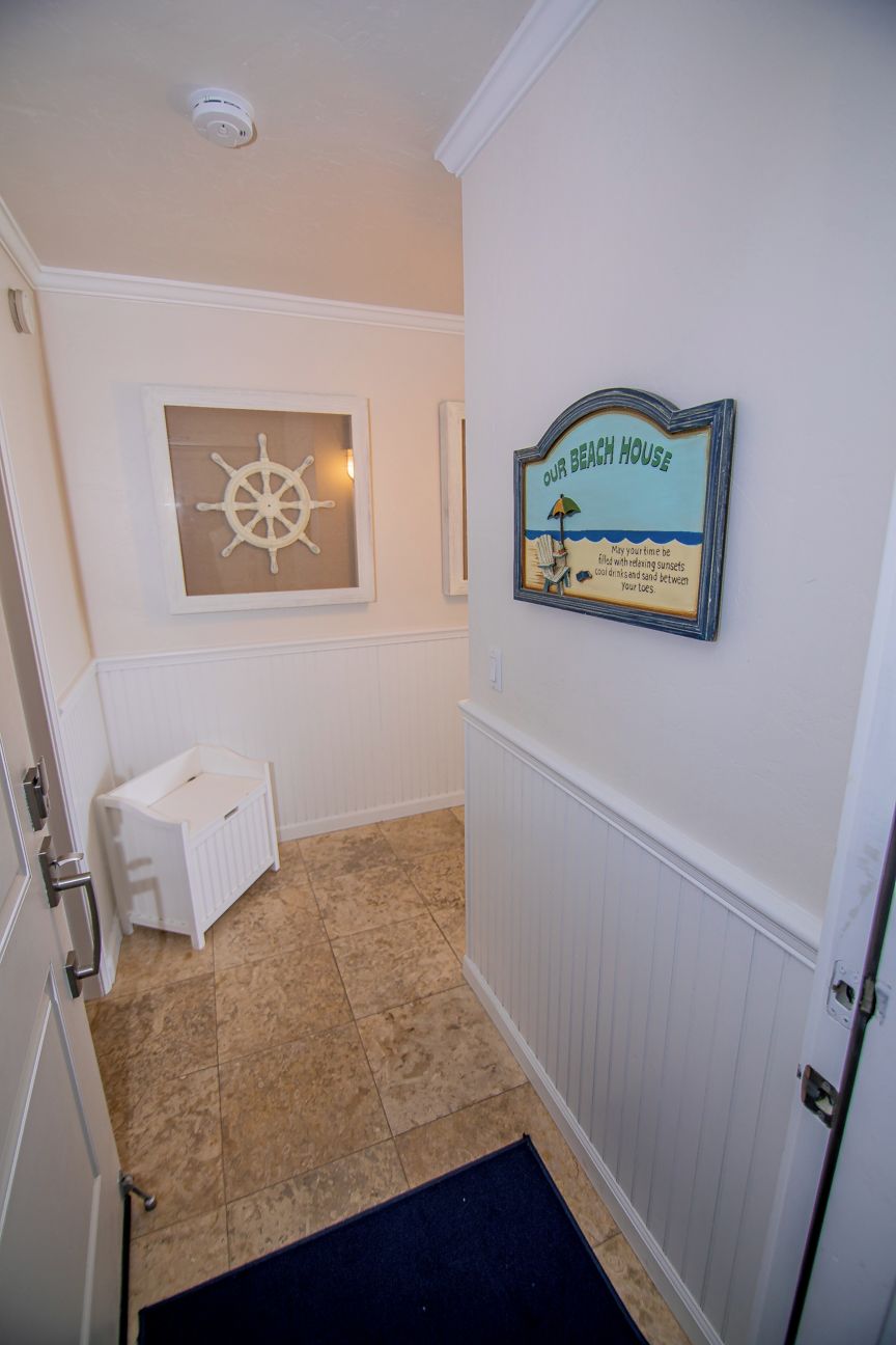 A hallway with a baby changing station, a framed nautical-themed sign, and a door with a doormat.