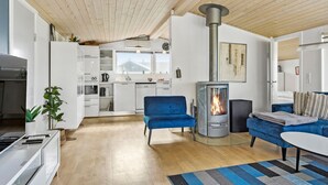 A modern living room with a wood-burning stove, a blue sofa, and a kitchen in the background. - 3 bedroom amazing home in Spøttrup (Spøttrup)