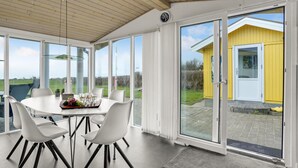 A dining area with a round table, white chairs, and a view of a yellow building through large glass doors. - 3 bedroom amazing home in Spøttrup (Spøttrup)