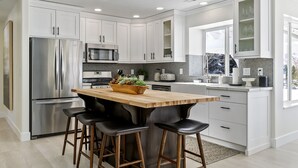 A modern kitchen with white cabinetry, stainless steel appliances, and a wooden island with bar stools.