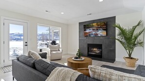 A modern living room with a grey sofa, a round coffee table, a fireplace, and a large TV mounted on the wall.