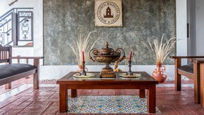 A room with a large ornate table, two potted plants, and a wall-mounted sign. - HONDA COLONIAL MAGDALENA RESORT (Honda)