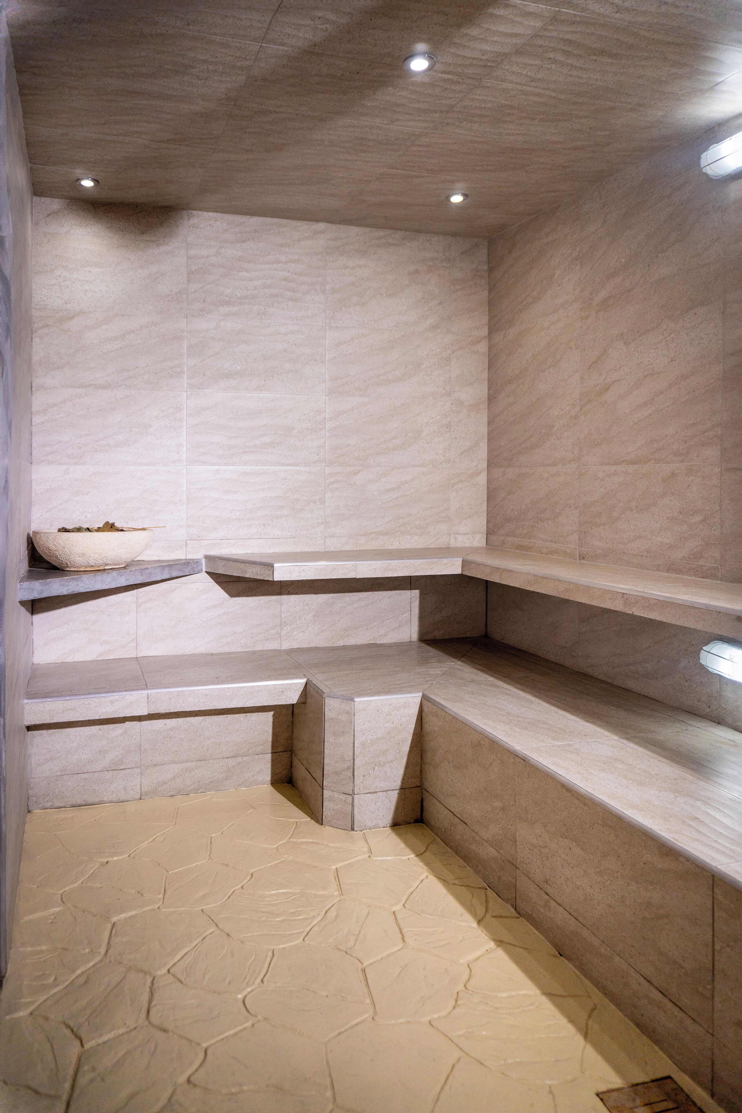 A modern bathroom with a geometric tile floor, recessed lighting, and built-in shelves.