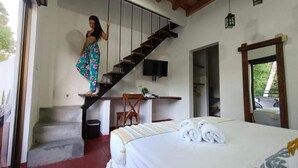 A bedroom with a bed, a desk, a chair, a staircase, and a TV. - HONDA COLONIAL MAGDALENA RESORT (Honda)