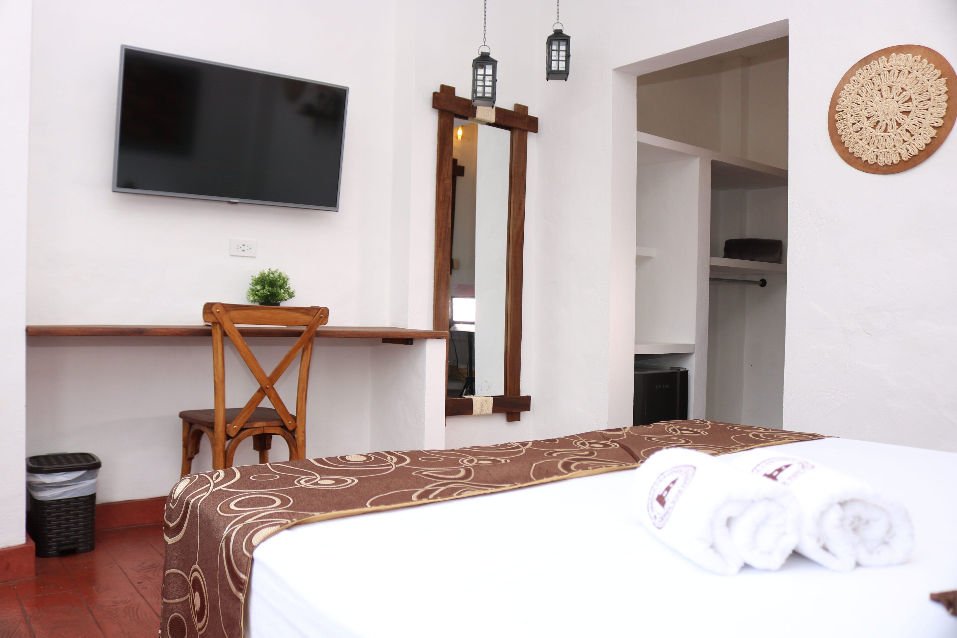 Habitación de hotel con cama, escritorio, silla, televisor y espejo.