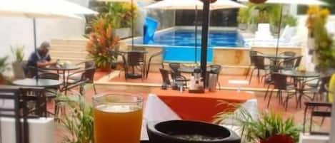 A tray with food and drinks, a pool, and outdoor seating in a hotel setting.