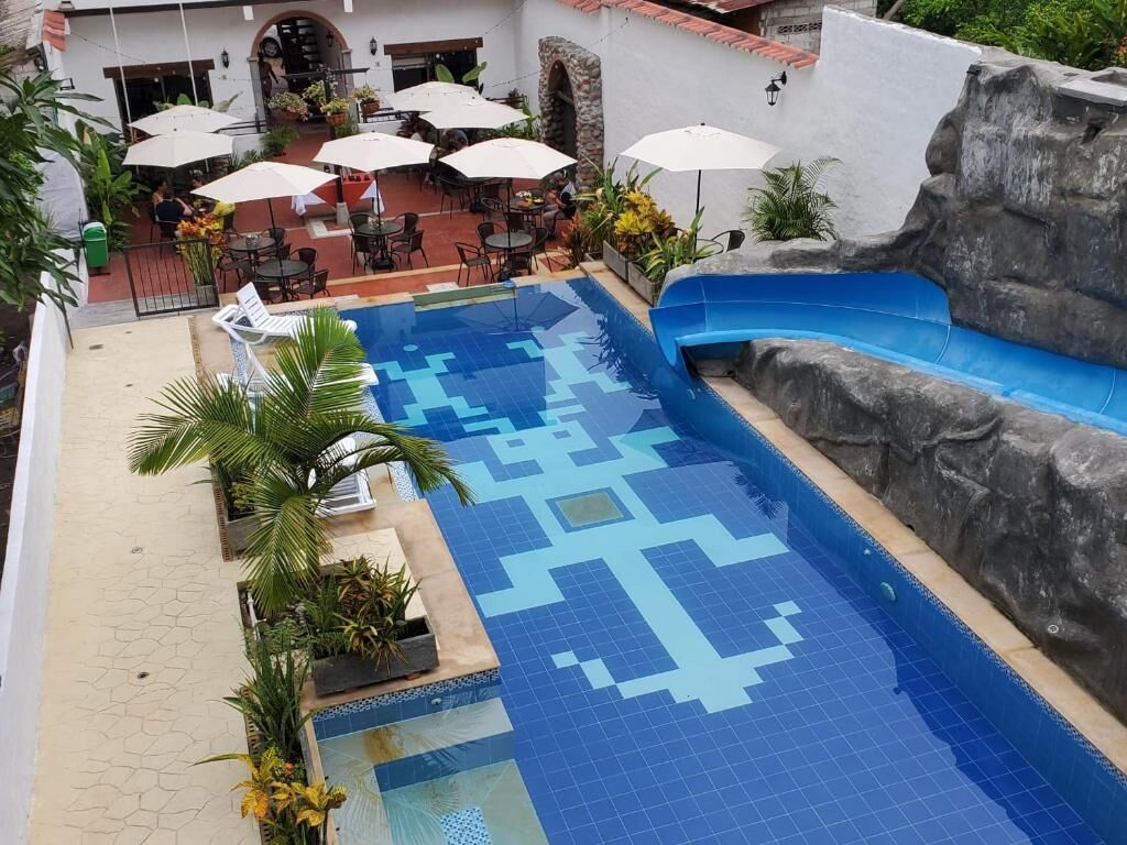 Una piscina con un diseño geométrico de azulejos, rodeada de sillones de playa y sombrillas, y una pared rocosa en un lateral.