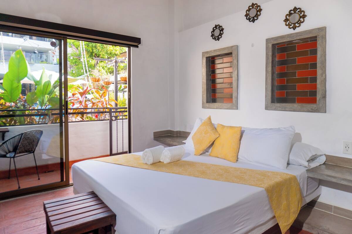 A hotel room with a bed, a bench, a chair, and a view of the outdoors through a sliding door.