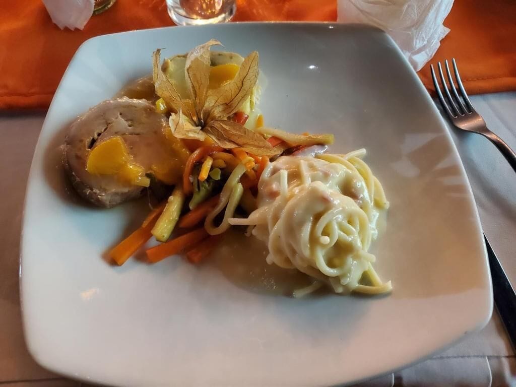 A plate with a rolled meat, vegetables, and pasta.