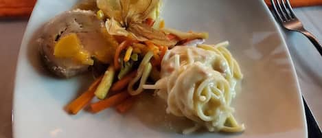 A plate with a rolled meat, vegetables, and pasta.
