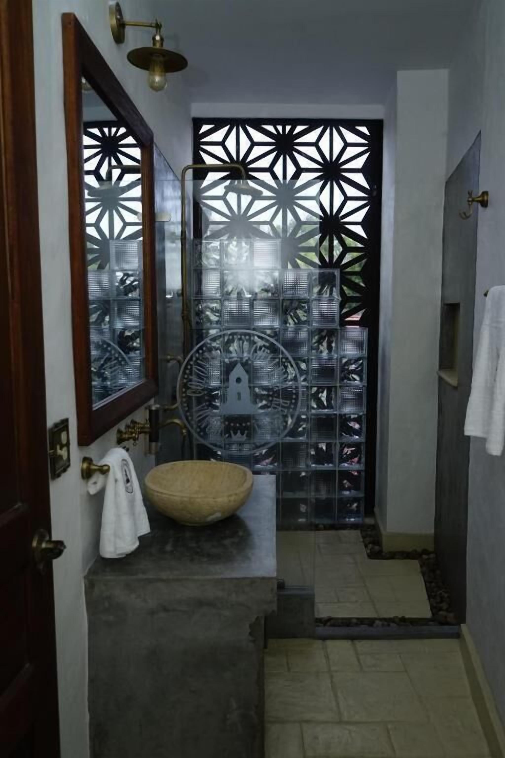 A bathroom with a large mirror, a round sink, and a decorative glass partition.