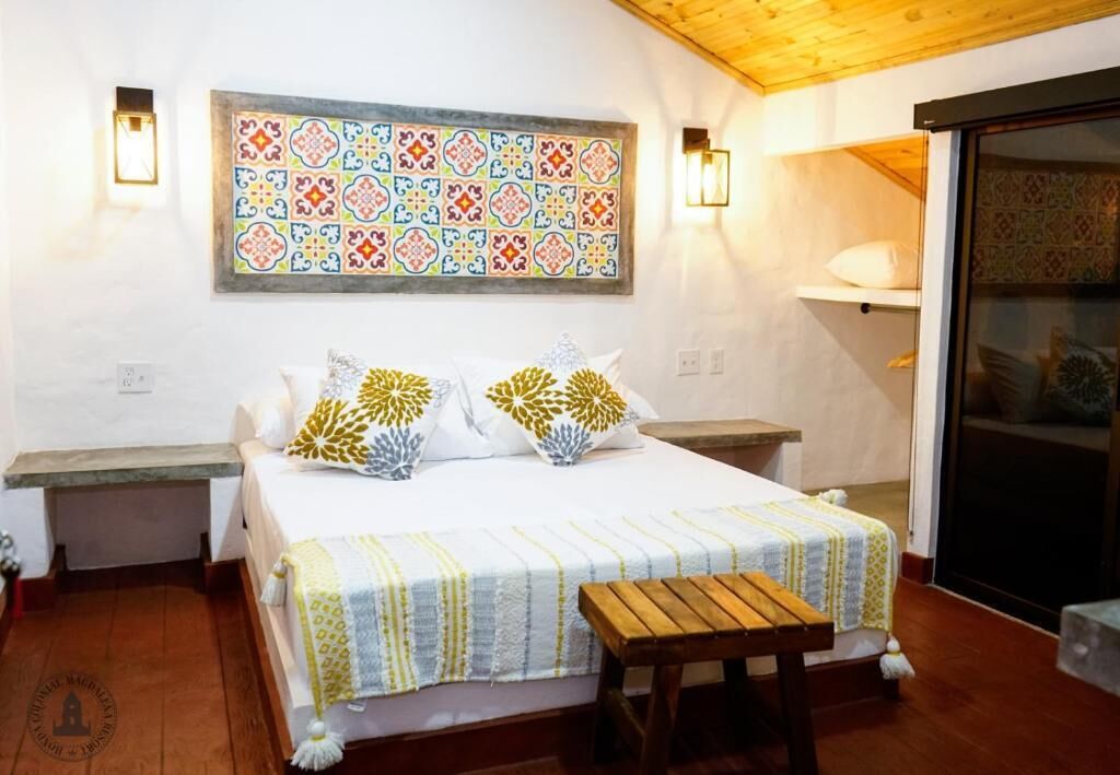 A bedroom with a bed, a wooden bench, a colorful tile wall, and a sliding door.