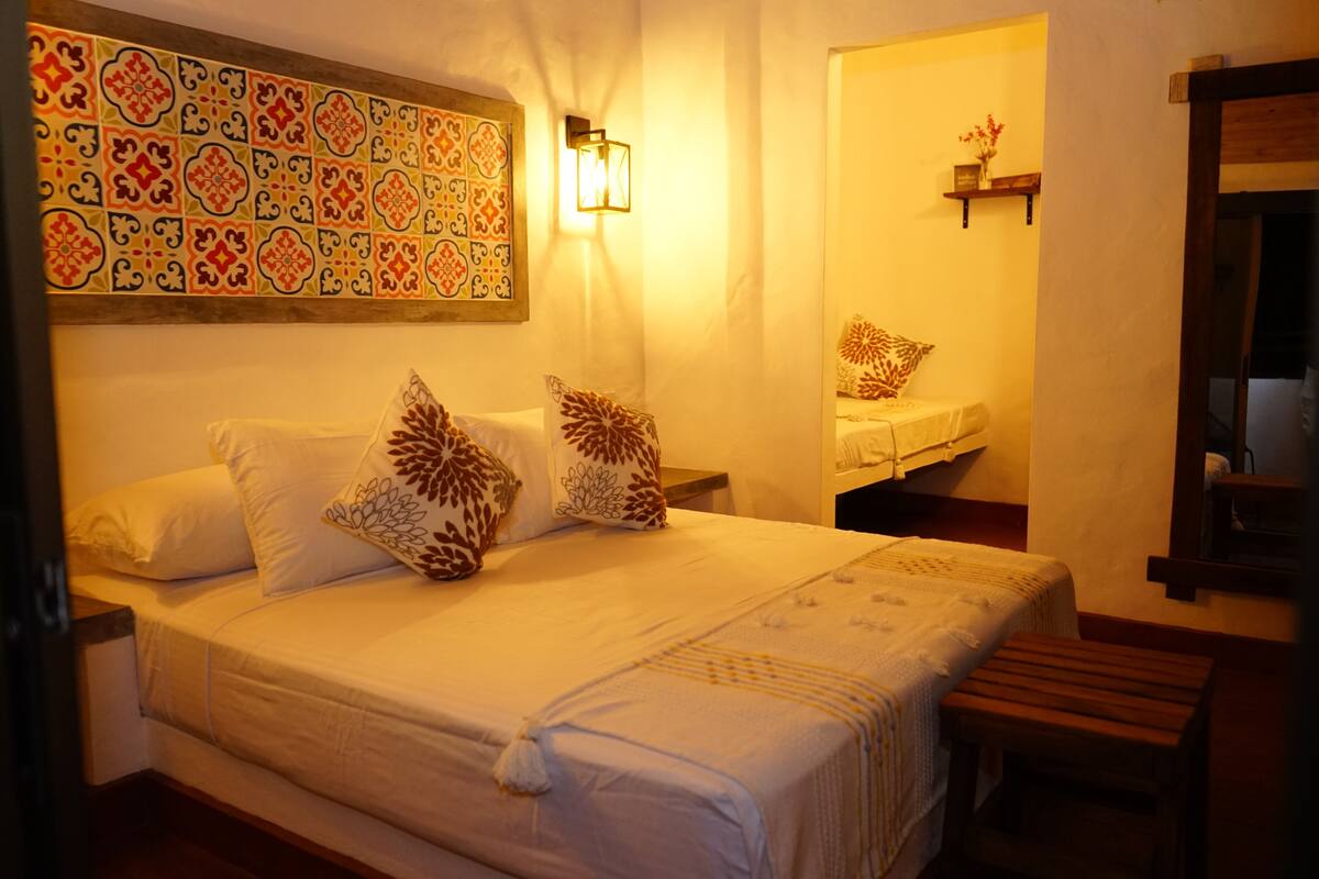 A neatly made bed with patterned pillows, a wall-mounted light fixture, and a small shelf with a vase.