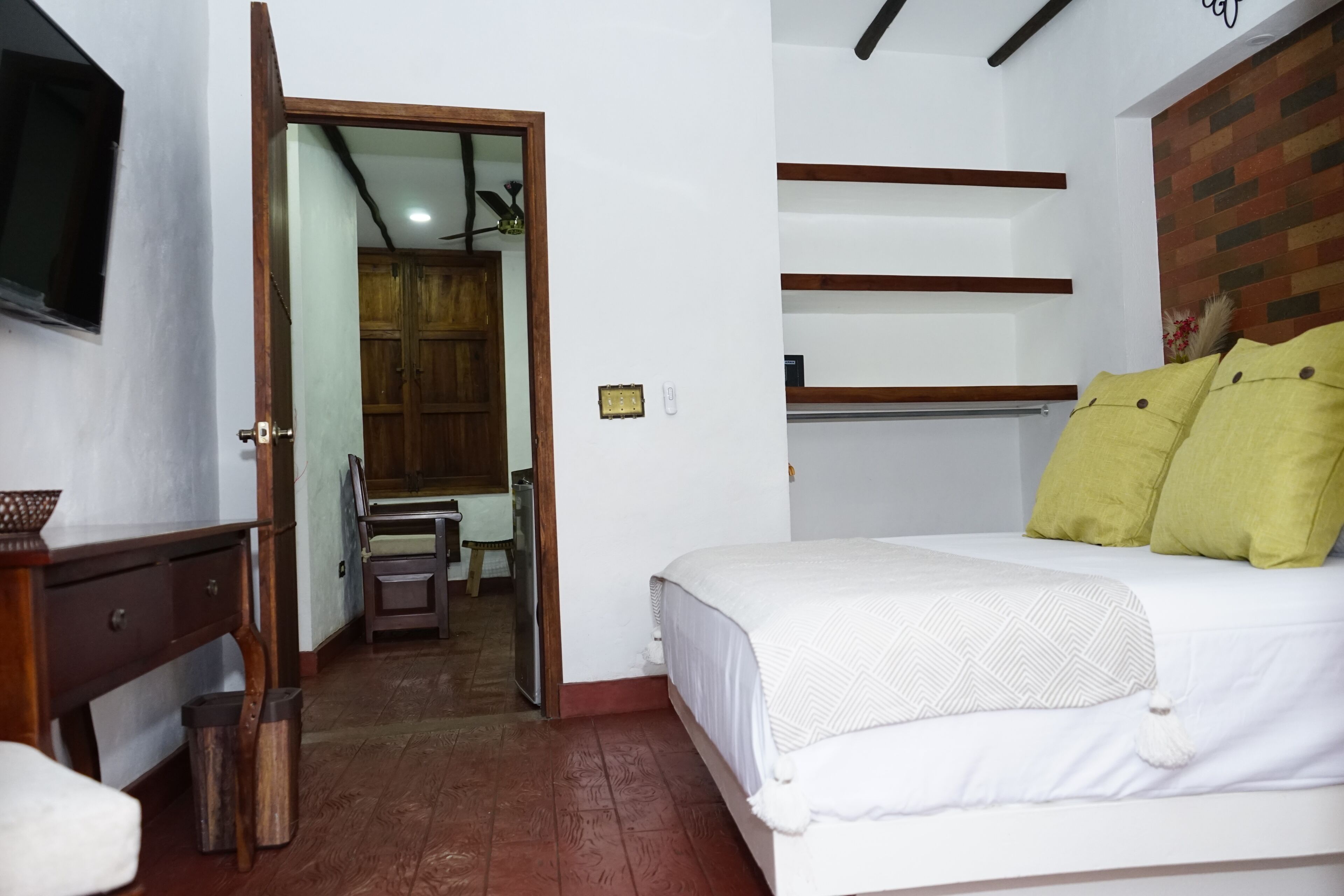 A bedroom with a bed, a wooden nightstand, a desk, and a chair. There is a wardrobe and a mirror in the background.