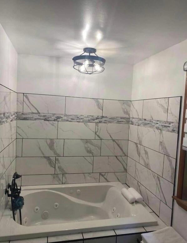 A modern bathroom with a freestanding bathtub, marble tiles, and a unique ceiling light fixture. - Tres Casa Lake House (Coloma)