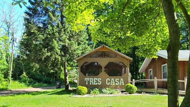 Una construcció de fusta amb la inscripció 'TRES CASA' envoltada de vegetació exuberanta.