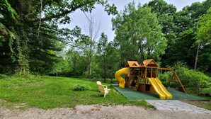 Un parc infantil amb tobogan i elements per escalar, envoltat d'arbres.