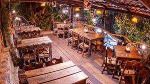 Een terras van hout buiten, met tafels en stoelen, omringd door weelderige begroeiing en een zwembad.