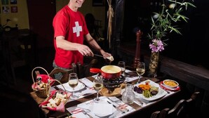 Een eettafel gedekt met verschillende gerechten, wijnglazen en een rode pan op een fornuis.