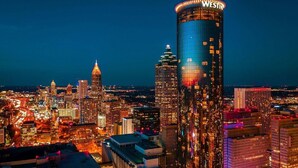 A cityscape at night with prominent high-rise buildings, including a hotel with a distinctive curved facade and illuminated signage. - Popular Filming Area- Downtown Atlanta Condo (atlanta)