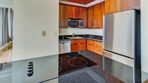 A modern kitchen with wooden cabinets, a stainless steel refrigerator, a microwave, and a black induction cooktop. - Popular Filming Area- Downtown Atlanta Condo (atlanta)