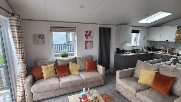 A modern living room with two sofas, a coffee table, and a kitchen area with a countertop and cabinets. - Honeycomb Lodge (Padstow)