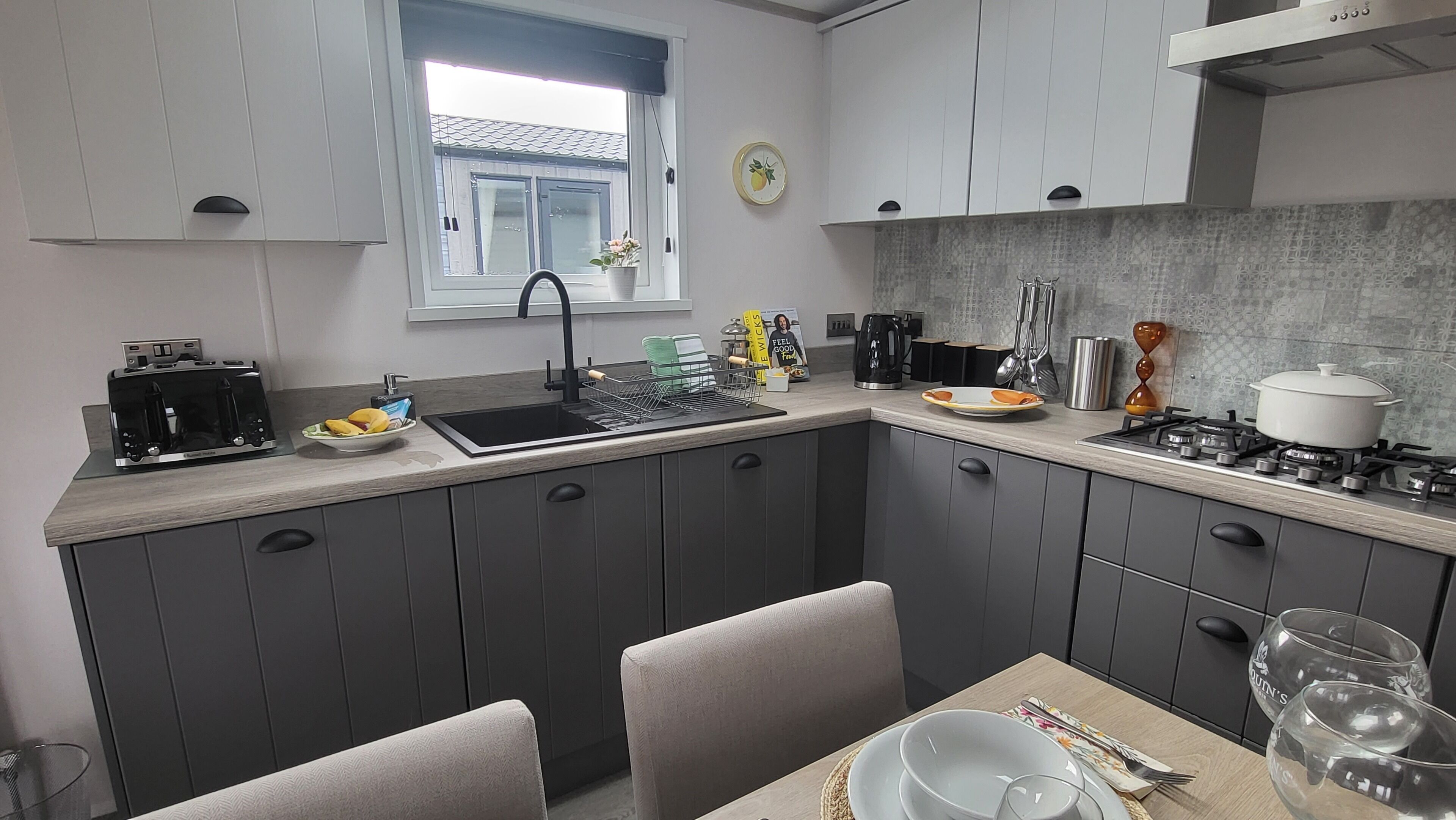 A modern kitchen with grey cabinets, a sink, a stove, and a dining area with a table and chairs.