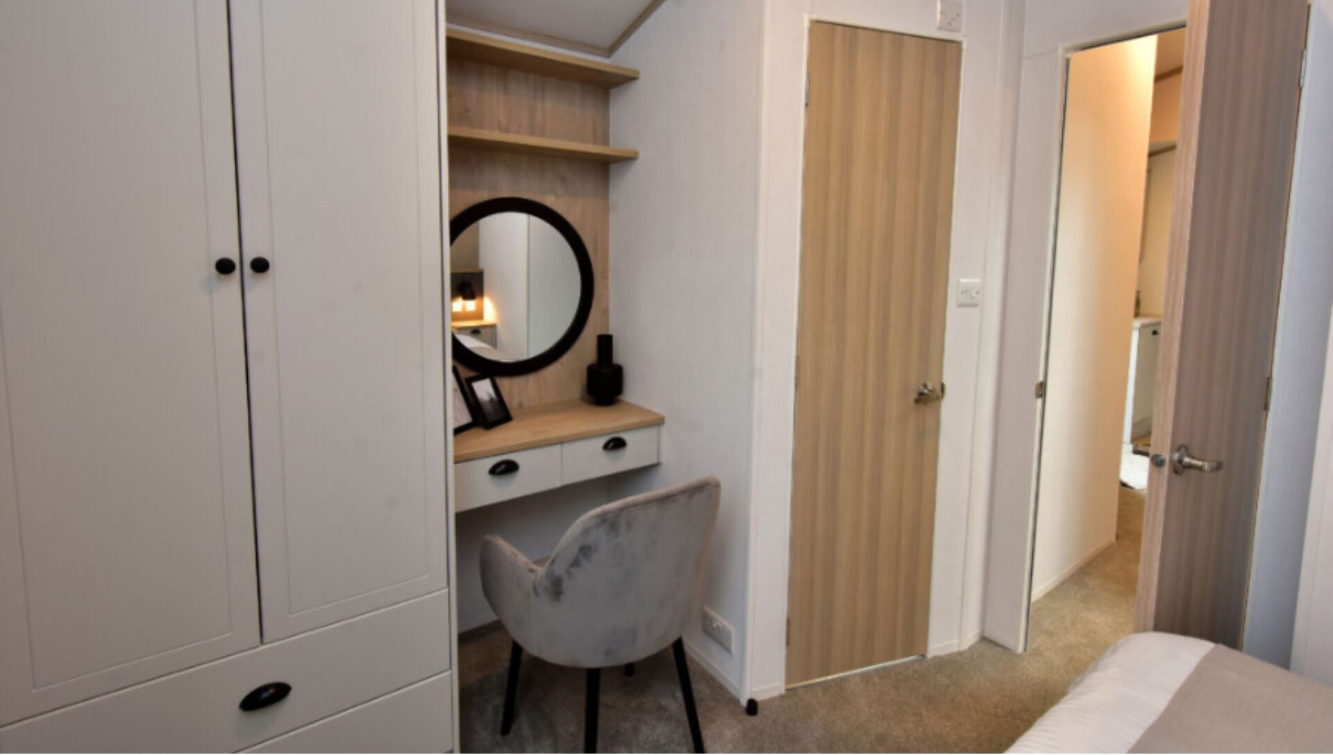 A bedroom with a bed, a desk with a chair, a wardrobe, and a door leading to another room.